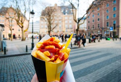 Brussels city guide.Belgian fries.01 A paper-bag with french fries in front of old houses in Brussels