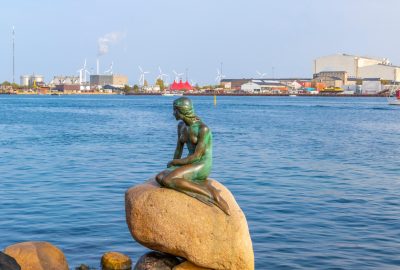 Copenhagen city guide.Little Mermaid statue.01 Little Mermaid statue in Copenhagen with sea and industrial area at the background