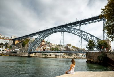 Porto city guide.Dom Luis I Bridge.02 Girl sitting at the bank of the Douro river and looking at the Bridge Dom Luis I in Porto