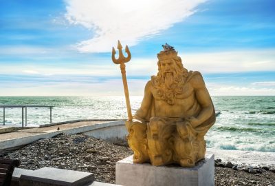 Sochi city guide.Neptune statue at Black Sea.01 Statue of Neptune with pigeons on his crown at a Sochi beach against backdrop of Black Sea